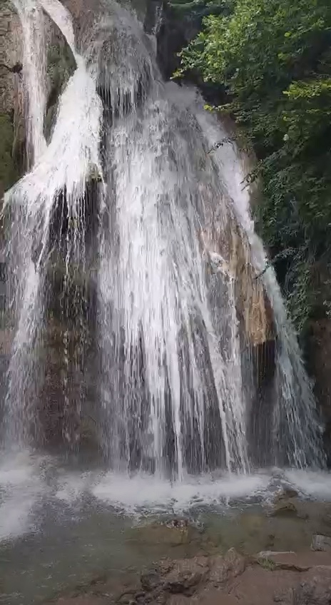 Красивый водопад. Крым. Водопад с прозрачной водой падает на камни среди зелёного леса.