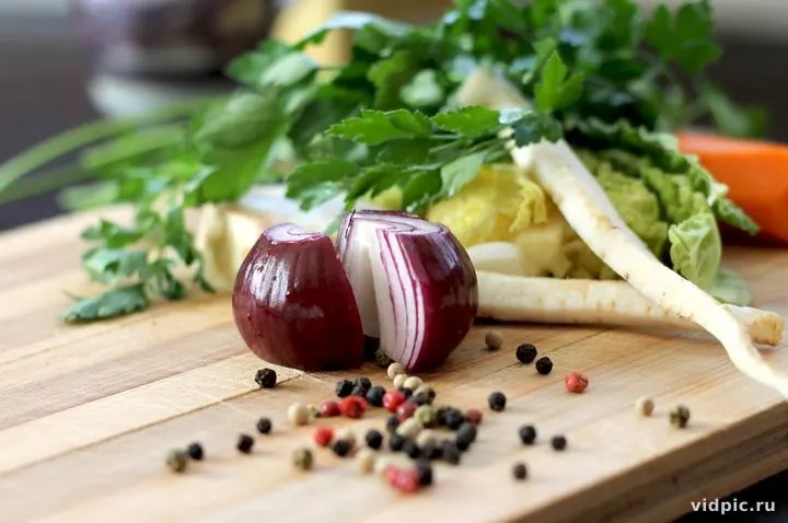 Red onion and herbs on a wooden cutting board. A wooden cutting board with a red onion, herbs, and pepper.