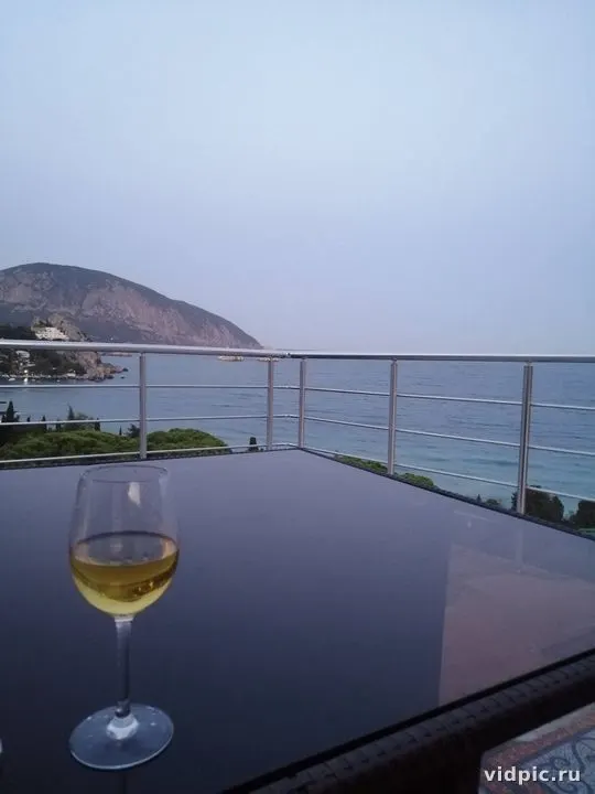 A glass of white wine against the backdrop of mountains and sea. A glass of white wine is on the table.