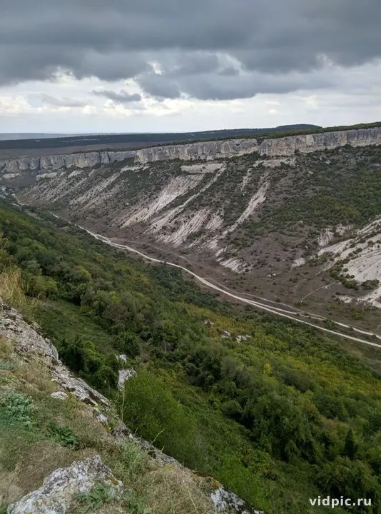 Mountains under cloudy sky with winding road. Green mountain slopes and a gray sky with clouds.