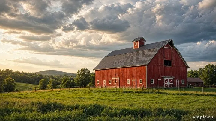 A classic red barn on a green field under clouds.
