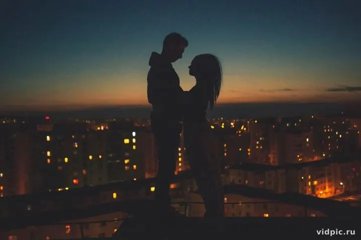 Silhouettes against the sunset over the city. A couple stands against the sunset, their silhouettes highlighted against the orange sky and city lights.