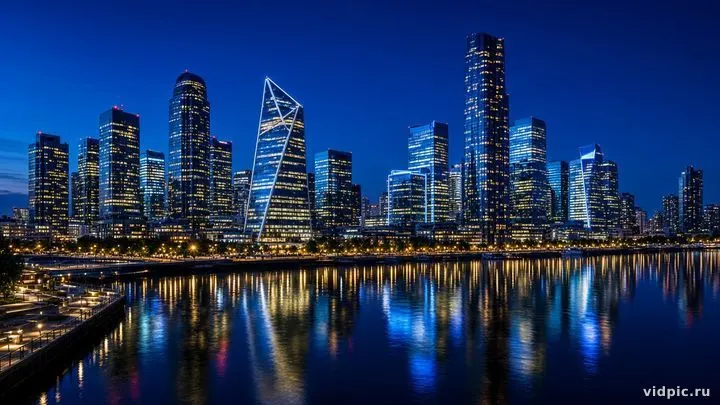 Skyscrapers and lights reflected in the river at blue hour.