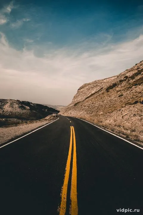Mountain road under cloudy sky. An asphalt road winds through hills under a gray, cloudy sky.