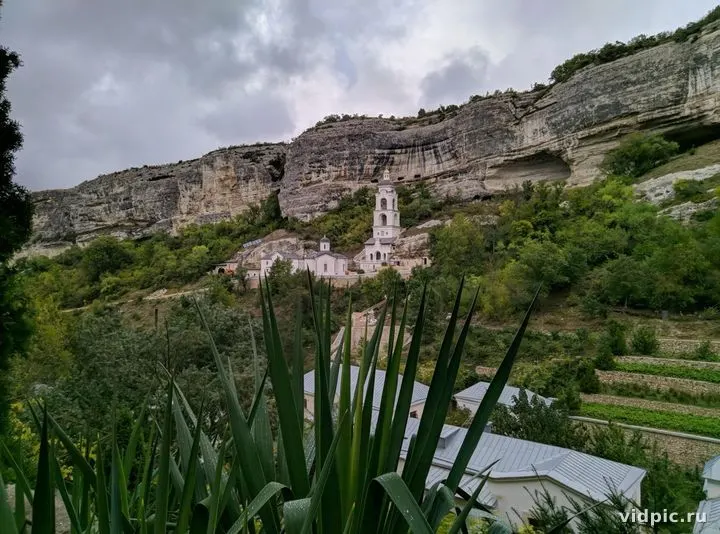 Church at the foot of the mountains under a cloudy sky. A church at the foot of the mountains, surrounded by green trees.